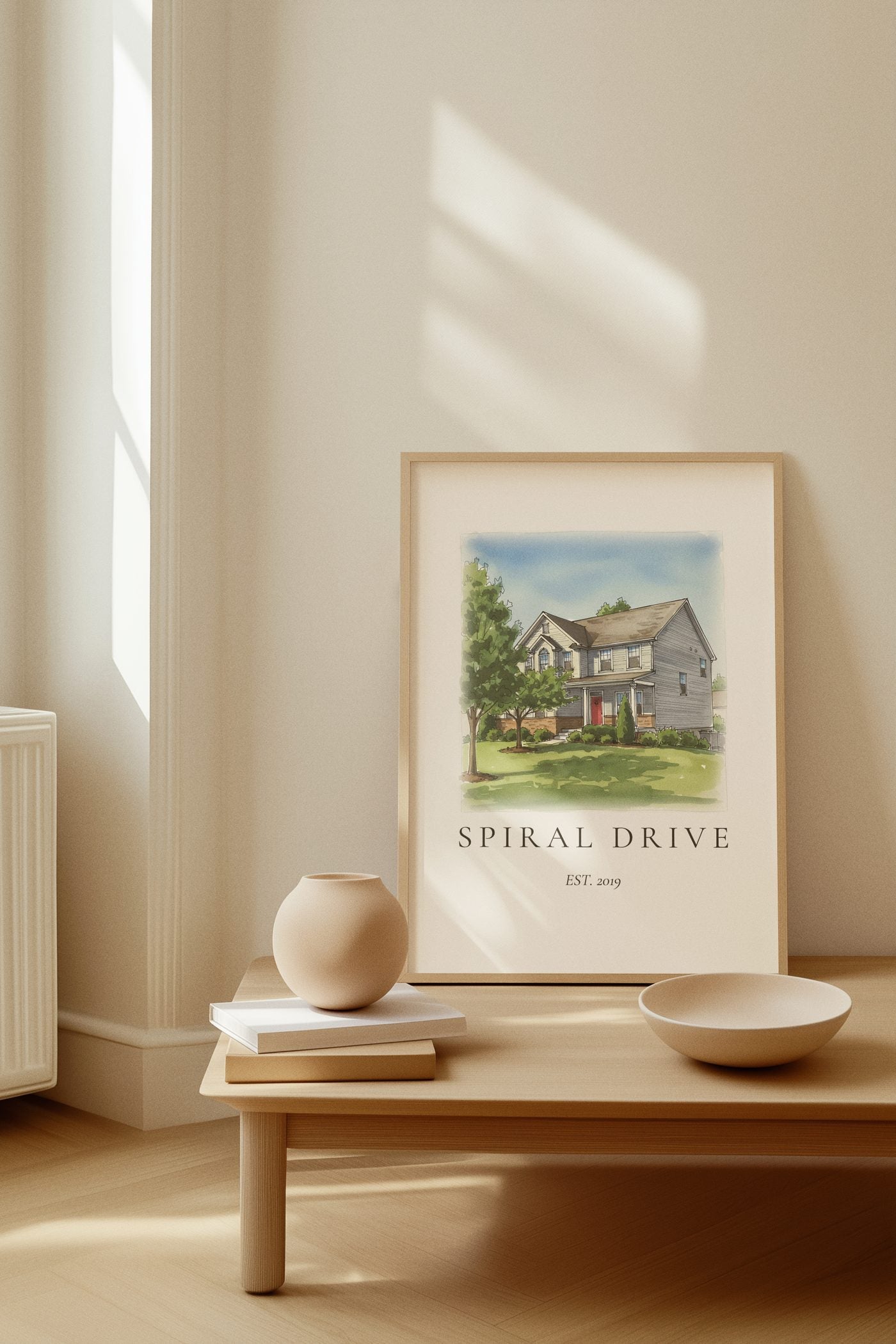 An ink and wash illustration of the Spiral Drive home, framed and leaning on a minimalist console table.